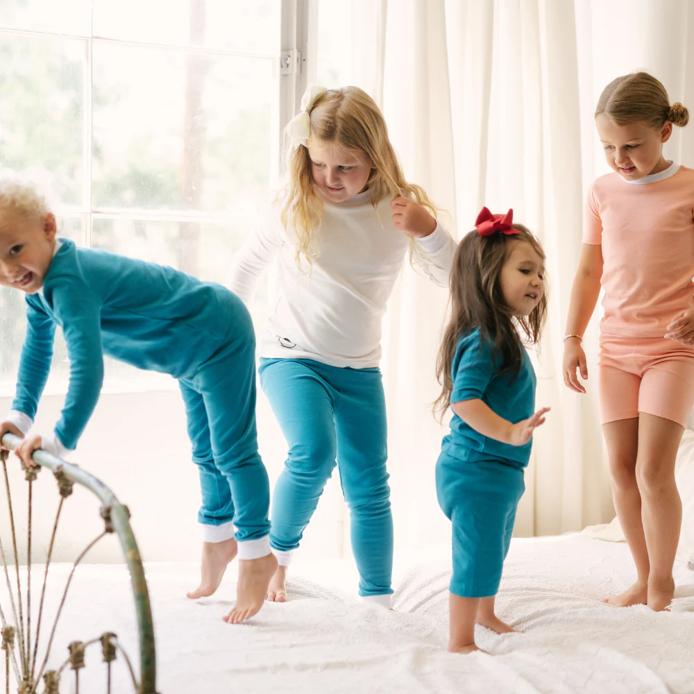 4 children jumping on a bed wearing incontinence pyjamas in blues and pinks